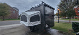 This dark gray Flyer off-road pop-up camper trailer with tent extension, ideal for RV rental adventures, is parked on a driveway.
