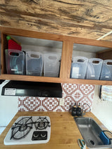 Compact RV rental kitchen with organized cabinets for cups, plates, and bowls, plus a stove and sink.