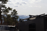 RV rental adventure: dark camper trailer with solar power, parked near pines with snowy mountains in the background.