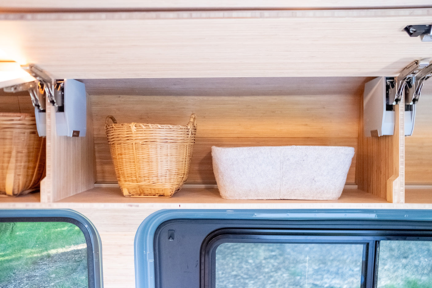 RV rental interior storage: organized wooden overhead cabinets with baskets, above blue-framed windows.