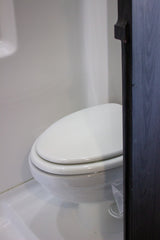 Inside an RV rental: a compact, white toilet with walls and flooring in matching white. Dark cabinet on right.