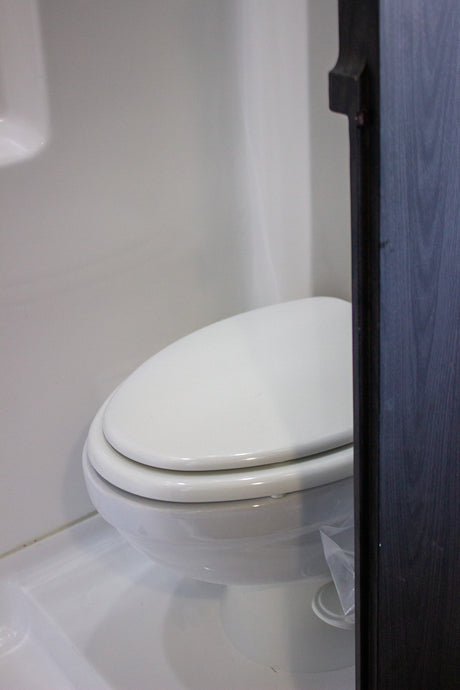 Inside an RV rental: a compact, white toilet with walls and flooring in matching white. Dark cabinet on right.