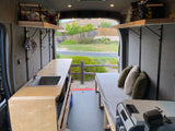 Bright RV rental interior: kitchenette with sink, cozy bed, and organized storage. Scenic outdoor view.