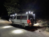 Illuminated 4x4 camper van & SUV parked on a dirt road at night, showcasing an RV rental for rugged outdoor adventures.