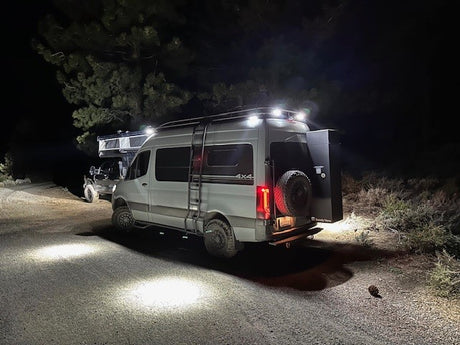 Illuminated 4x4 camper van & SUV parked on a dirt road at night, showcasing an RV rental for rugged outdoor adventures.