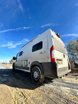 This dirty white Winnebago Solis RV rental stands on a muddy off-road trail under a clear blue sky, ready for adventure.