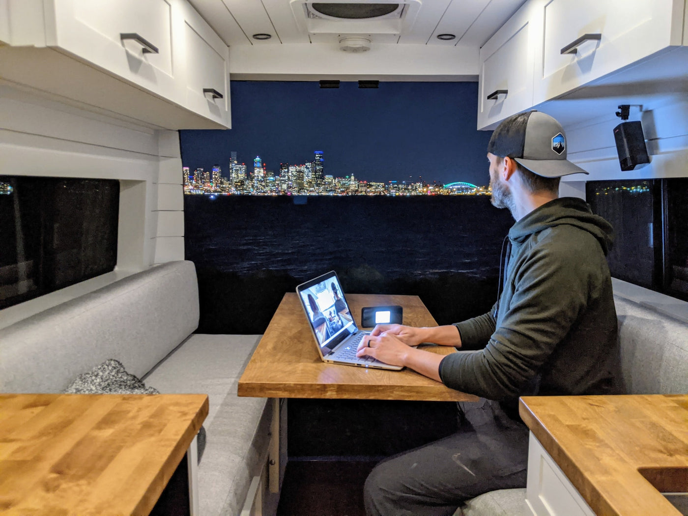 Man in an RV rental works on his laptop, enjoying a stunning city skyline view across the water at night. — photo 17