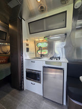 Modern RV rental kitchen with sink, stove, microwave, fridge, and a peek into the cozy bedroom.