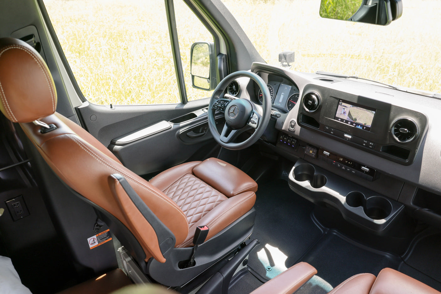 Explore in comfort! This rv rental's sleek van interior features brown leather seats, modern dashboard, & infotainment screen.