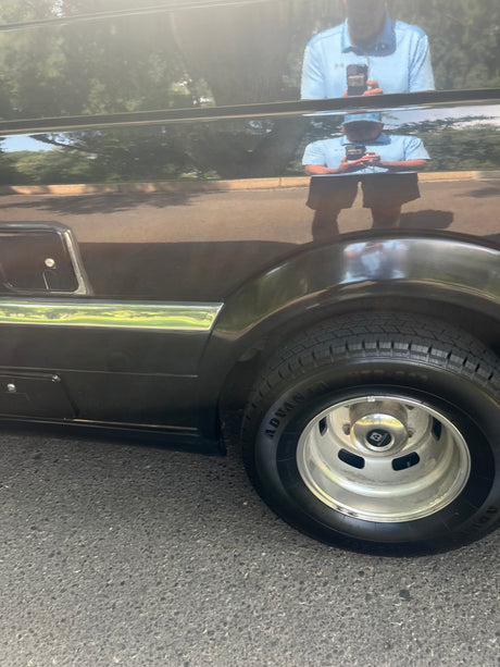 A shiny dark RV side, with its tire and reflections of a person & trees. Perfect for an RV rental.