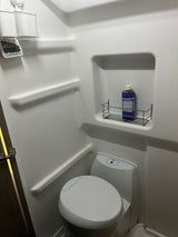 Compact RV rental bathroom with a white toilet, shower, and useful shelving holding Dr. Bronner's soap. Ideal for trips.