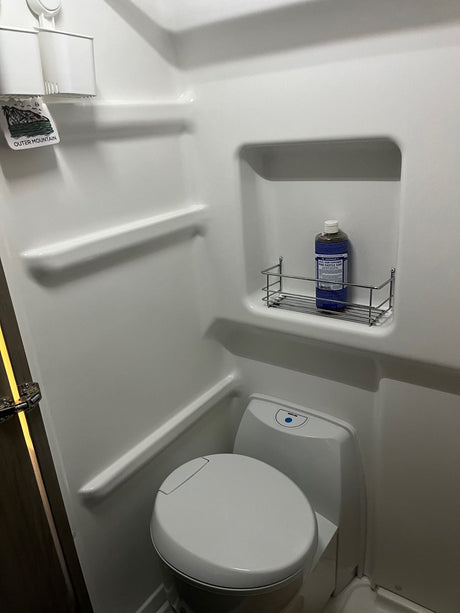 Compact RV rental bathroom with a white toilet, shower, and useful shelving holding Dr. Bronner's soap. Ideal for trips.