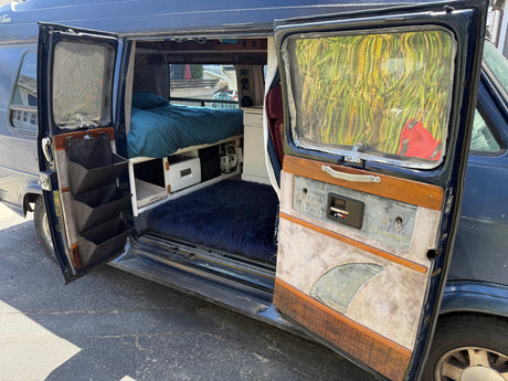 Step into adventure! This RV rental showcases its cozy, custom interior with a bed, smart storage, and a fluffy rug.