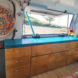 Inside an **rv rental**: custom wood & blue storage, open hatch with scenic outdoor view.