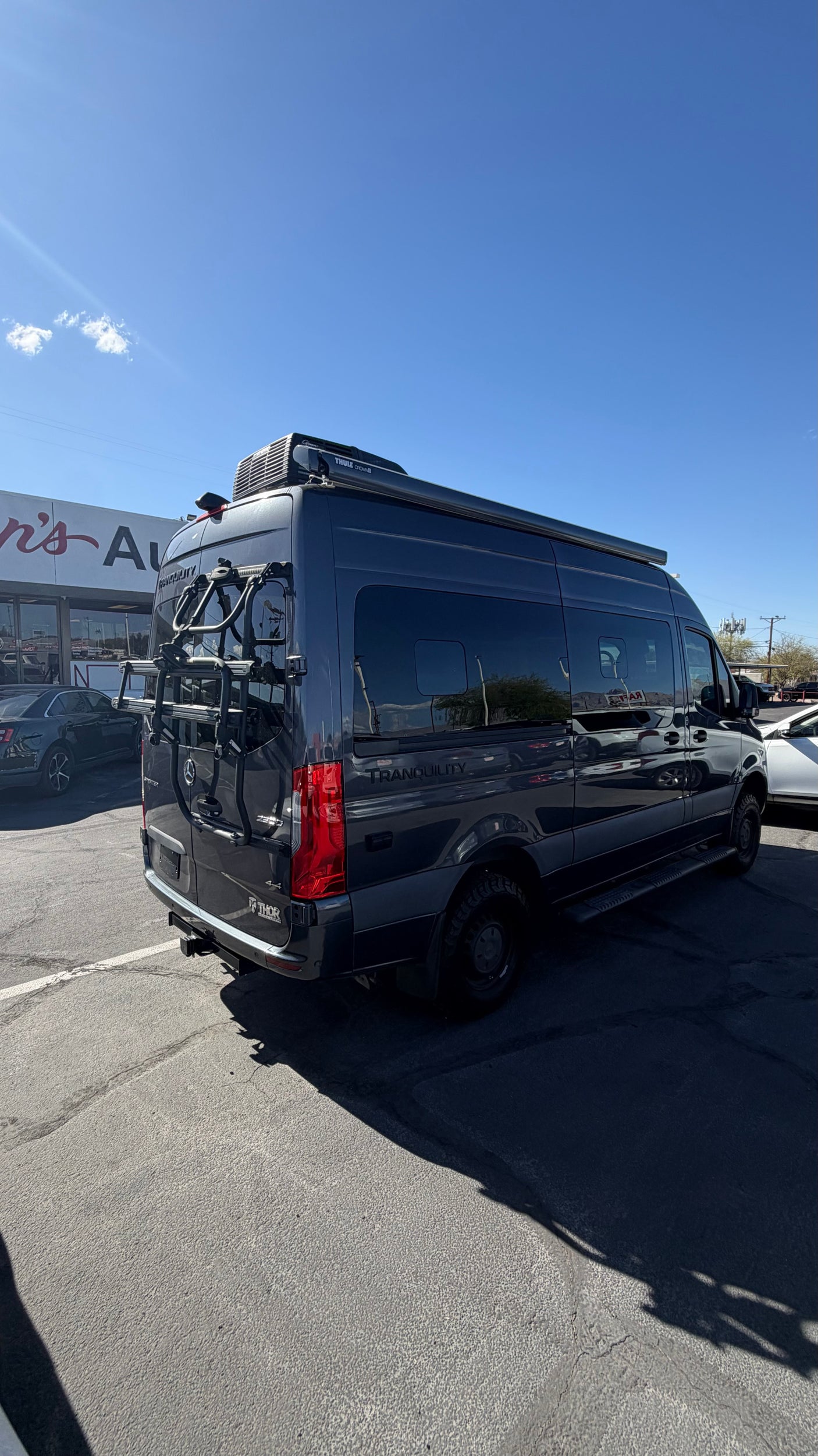 Dark gray Mercedes Sprinter Thor Tranquility rv rental camper van with a bike rack, parked outdoors on a sunny day.