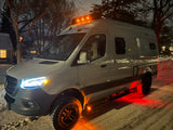 White camper van (rv rental) with bright lights on snowy night. Red underglow illuminates rugged tires, perfect for winter adventures.