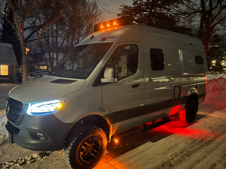 White camper van (rv rental) with bright lights on snowy night. Red underglow illuminates rugged tires, perfect for winter adventures.