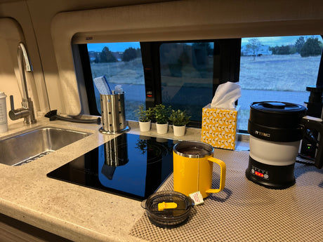 Functional rv rental kitchen counter with a sink, cooktop, tea mug, electric kettle, and a view.
