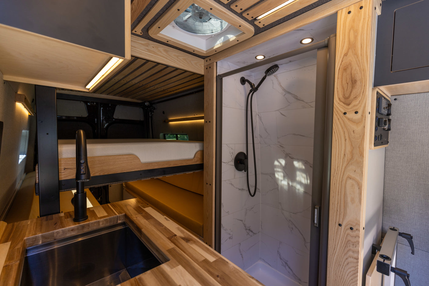 Inside a custom RV rental: wood kitchen, upper bed, and tiled shower. Explore comfortably in this campervan.