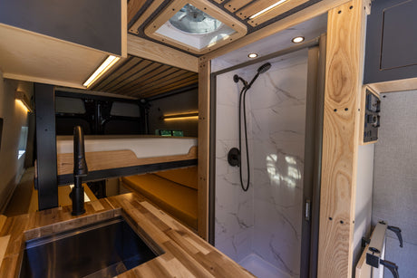 Inside a custom RV rental: wood kitchen, upper bed, and tiled shower. Explore comfortably in this campervan.