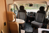 Interior of a modern RV rental, featuring swiveling front seats, dashboard, and a compact dining area.