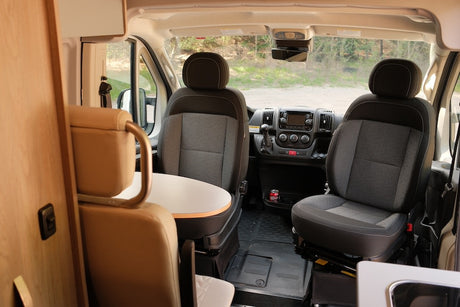 Interior of a modern RV rental, featuring swiveling front seats, dashboard, and a compact dining area.