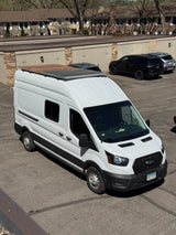 White Ford Transit camper van, possibly an rv rental, parked in a lot with solar panels and a roof deck.