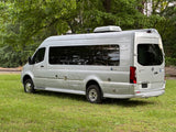 Silver Airstream Interstate touring coach RV parked on grass near tracks, great for rv rental.