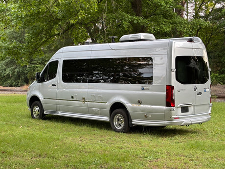 Silver Airstream Interstate touring coach RV parked on grass near tracks, great for rv rental.