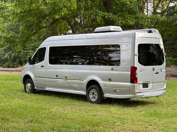 Silver Airstream Interstate touring coach RV parked on grass near tracks, great for rv rental.