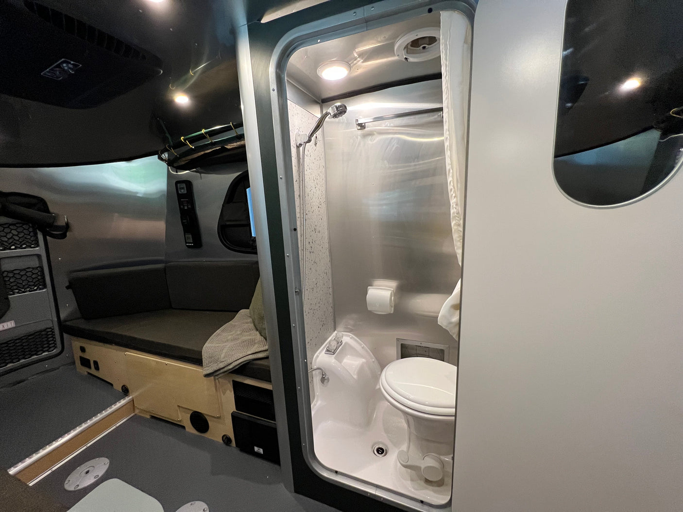 Compact RV rental interior: View of the wet bath with toilet and shower, plus a cozy living/sleeping area.