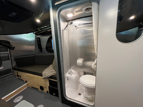 Compact RV rental interior: View of the wet bath with toilet and shower, plus a cozy living/sleeping area.