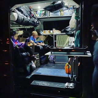 Cozy camper interior! Two kids relax inside their bright **RV rental**, featuring compact kitchen & storage for family van life camping.