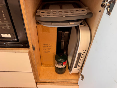 RV rental kitchen cabinet reveals compact storage: collapsible items, a propane tank, and a microwave.