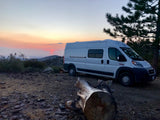 A white RV rental camper van parked on a dirt road, overlooking a vibrant mountain sunset.