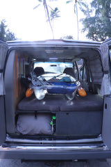 RV rental interior featuring organized gear storage, a convertible bed, and a sunny view of palm trees, ideal for travel adventures.
