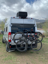Silver RV rental with mountain bikes parked by a lake, snowy mountains in the background. Ready for adventure!