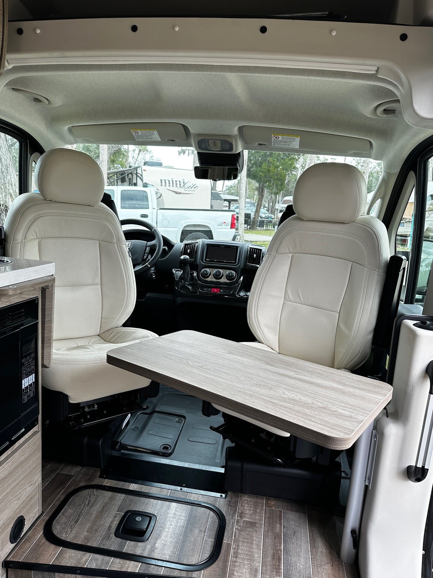 Modern rv rental interior features cream seats, a functional table, and wood-look flooring for comfortable travel.