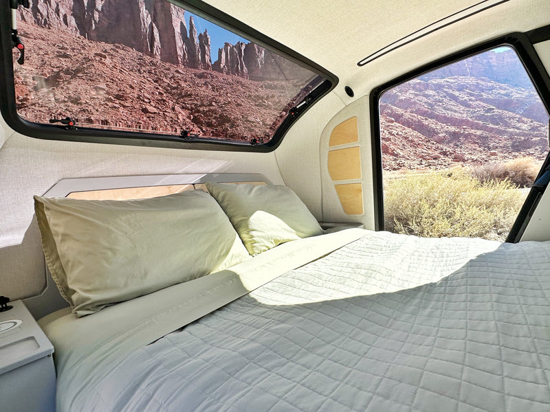 Serene RV rental interior with a comfy bed and large windows revealing dramatic red rock and desert landscapes outside. — photo 4