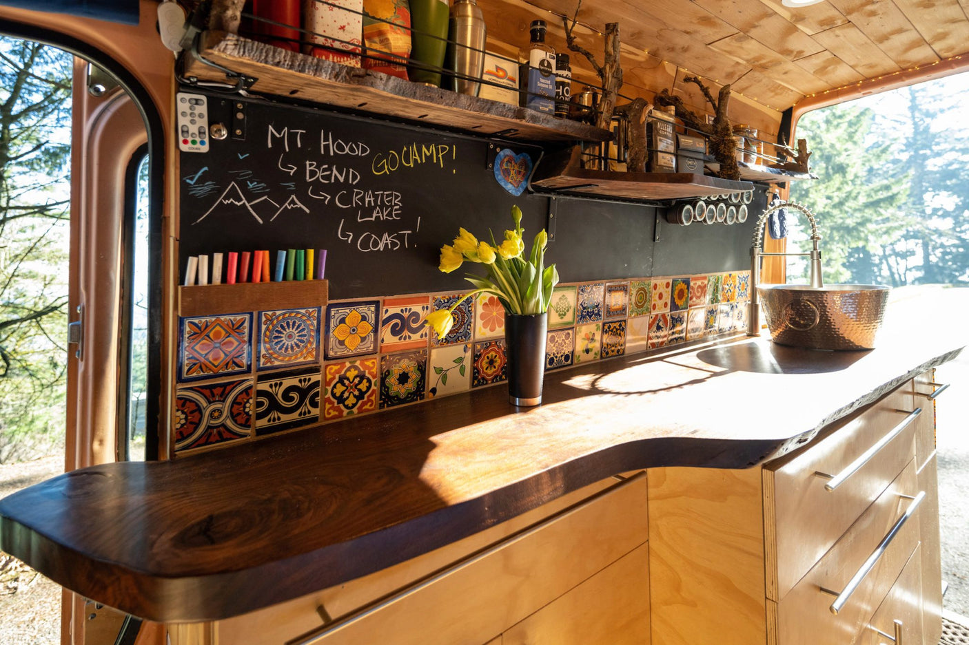 Cozy RV rental kitchen featuring a dark wood counter, vibrant tiled backsplash, and a chalkboard wall with travel plans.