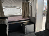 Inside an RV rental: a pop-up camper with a comfy bed, small kitchen, and storage, ideal for compact travel.