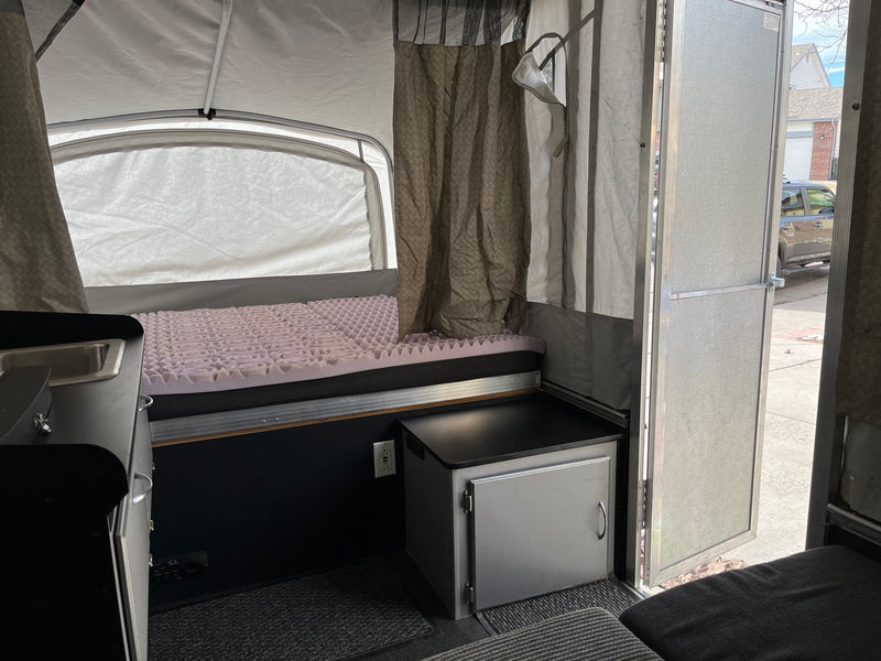 Inside an RV rental: a pop-up camper with a comfy bed, small kitchen, and storage, ideal for compact travel. — photo 9
