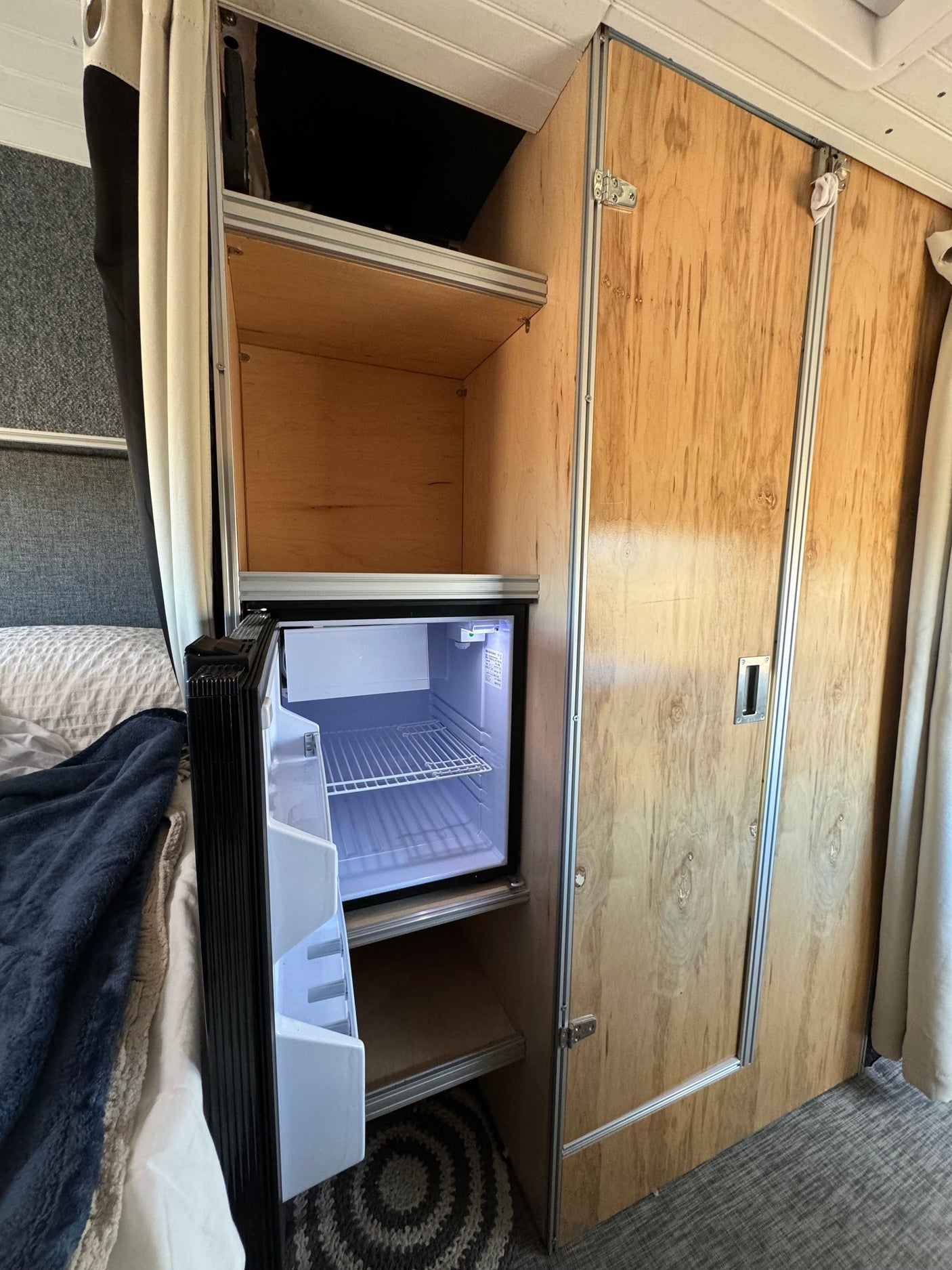 Inside an RV rental: compact fridge, open shelving, and wood-paneled storage. Essential for camper van life.