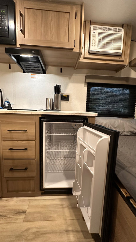 RV rental kitchen with a mini-fridge, microwave, hood vent, and AC unit. Compact and functional interior.