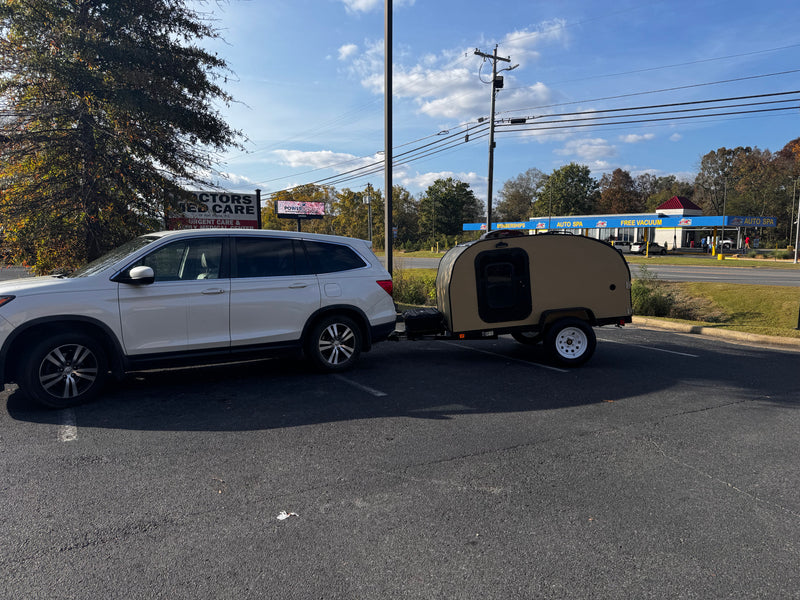 White SUV hitched to a tan teardrop RV rental, parked in a lot near an auto spa and medical center. — photo 7