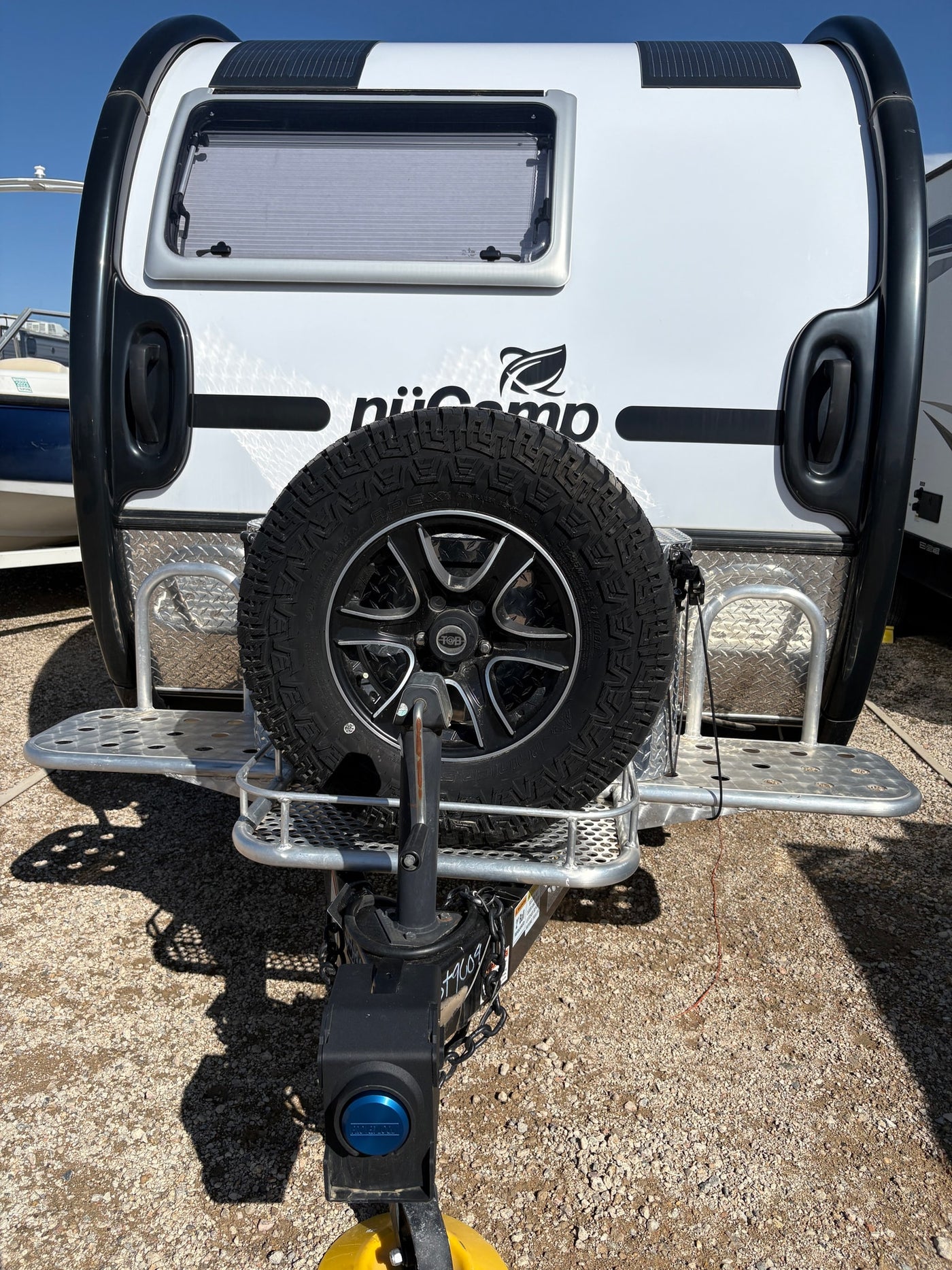 An RV rental option: a white nüCamp T@B travel trailer with a front-mounted spare tire on a gravel lot. — photo 2