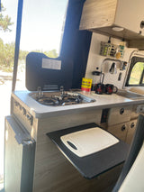 Compact RV rental kitchen featuring a gas stove, sink, coffee station, and extension counter, ideal for travel.