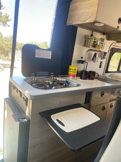 Compact RV rental kitchen featuring a gas stove, sink, coffee station, and extension counter, ideal for travel.