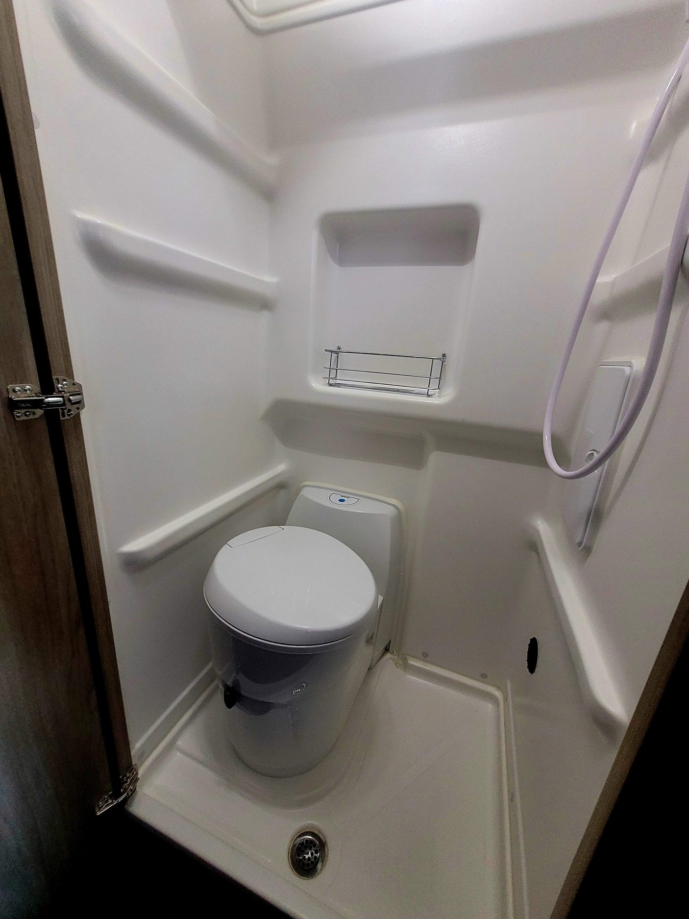 RV rental: Compact RV wet bath with white toilet, shower, and floor drain.
