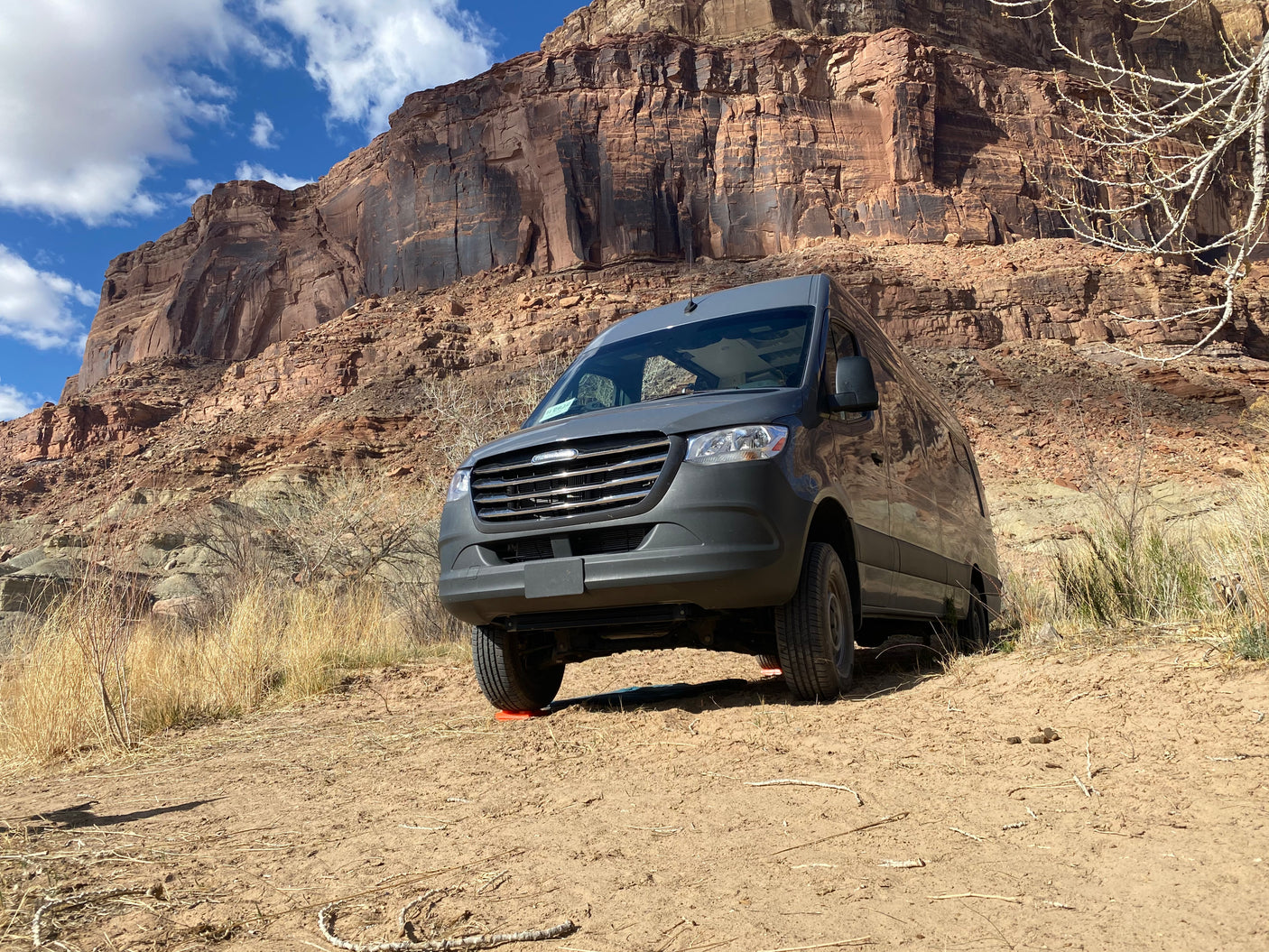Grey RV rental parked on dirt, towering red cliffs & blue sky. Perfect for desert road trips!